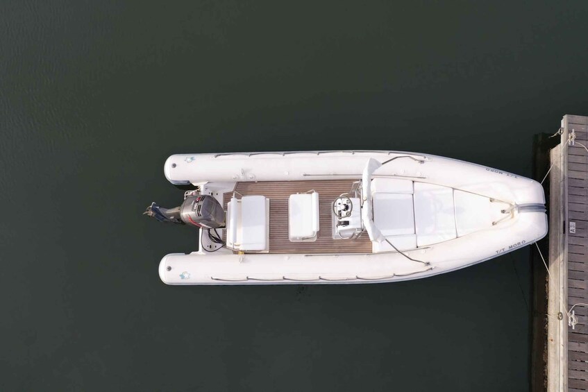 A white motorboat docked at a pier with a wooden deck and a motor in the foreground. 3