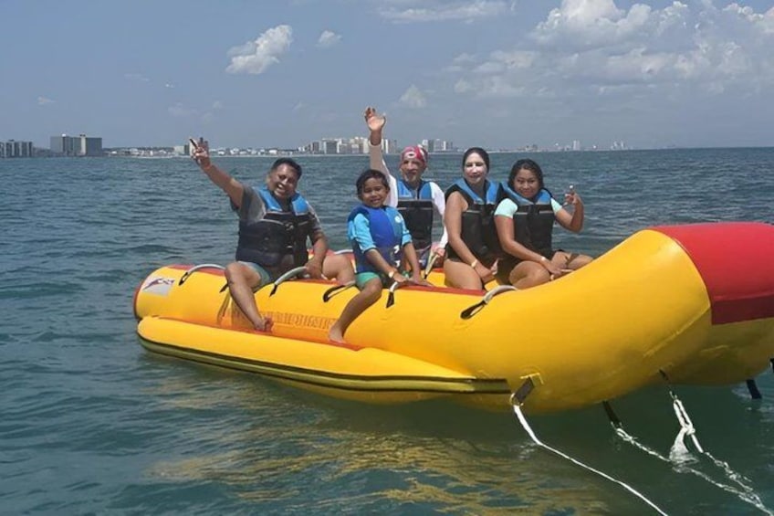 A group of people on a yellow inflatable raft in the water with a city skyline in the background. 2