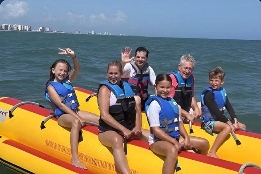A group of people on a yellow inflatable raft in the water with a city skyline in the background. 1