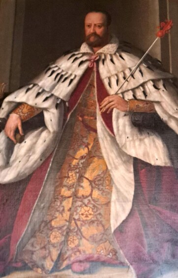 A person in a historical robe with a patterned garment and a staff. 4