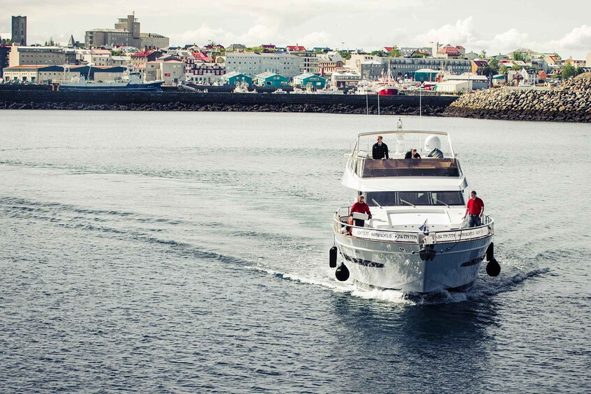 A white boat with two levels, moving through a calm body of water with a cityscape in the background. 4