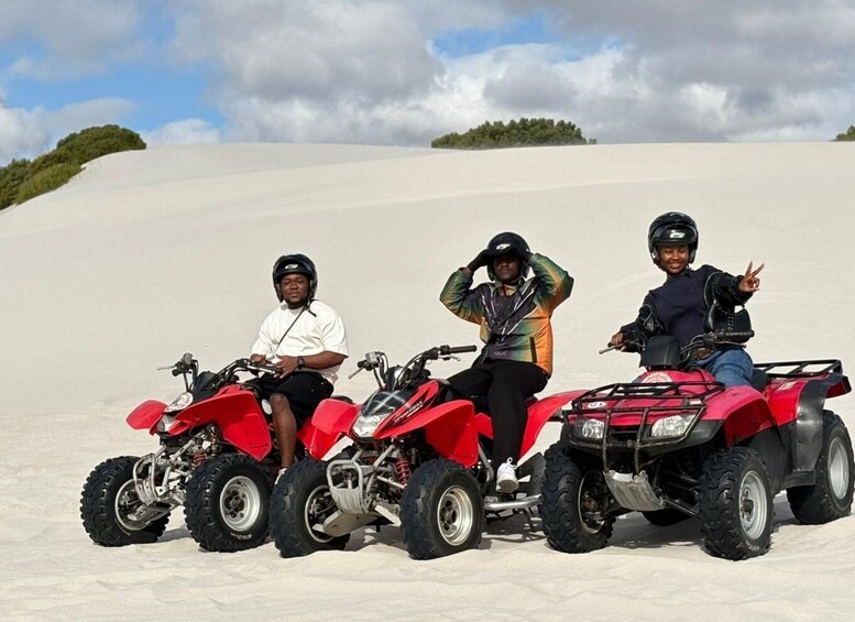 Three people on red quad bikes in a sandy area with sparse vegetation and a cloudy sky. 1