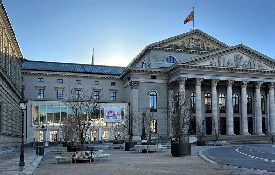 A classical building with columns, a flag, and a sign that reads 'MUNICH IST IMMER FIKTION.' 3