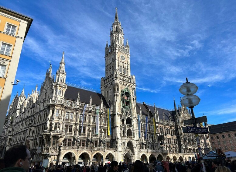 A historic building with intricate architecture, a prominent clock tower, and a bustling crowd in front. 1