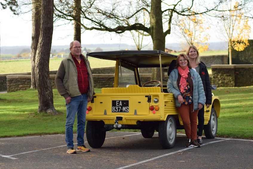 A yellow vehicle with a license plate on a paved road with trees and grass in the background. 1