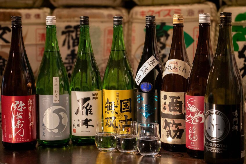Différentes bouteilles de saké japonais, avec leurs étiquettes, et des verres disposés devant. 1