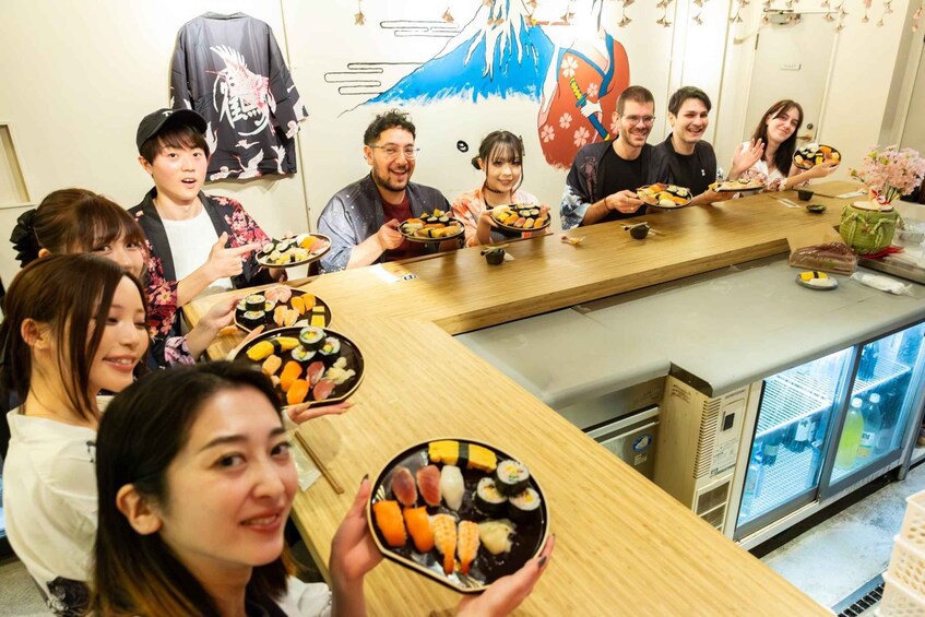 Un groupe de personnes tenant des assiettes de sushis dans un restaurant où est accrochée une peinture représentant une montagne. 3