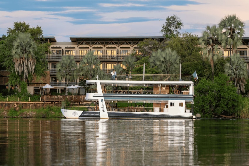 A houseboat docked near a building with balconies and palm trees. 2