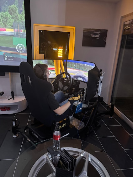 A person in a racing simulator cockpit with a steering wheel and pedals, surrounded by racing screens and a trophy on a table. 5