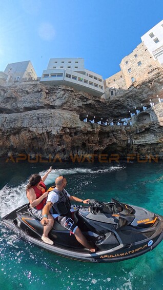 A jet ski on clear turquoise water with rocky cliffs and white buildings in the background. 3