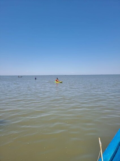 Calm sea water with a clear sky, a small boat with a person in the distance, and another boat further away. 5