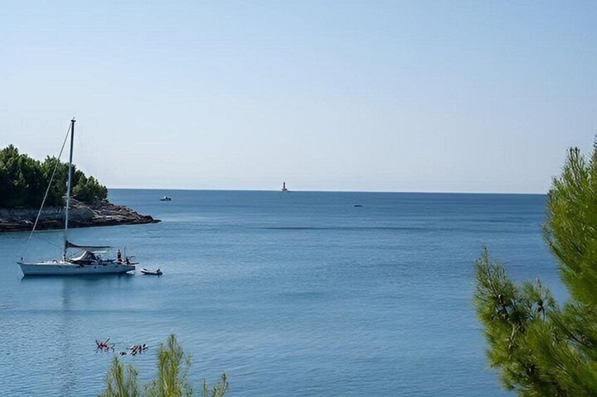 Une mer calme avec un voilier ancré près du rivage, entouré de verdure et d’un phare situé au loin. 2