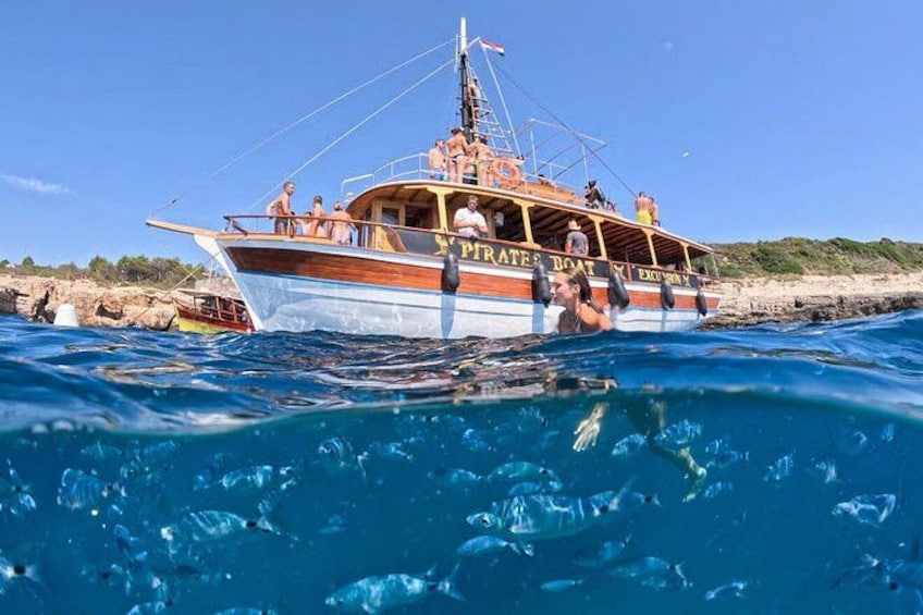 A boat named 'Pirate's Boat' with people on board, surrounded by clear blue water and rocky shoreline. 1