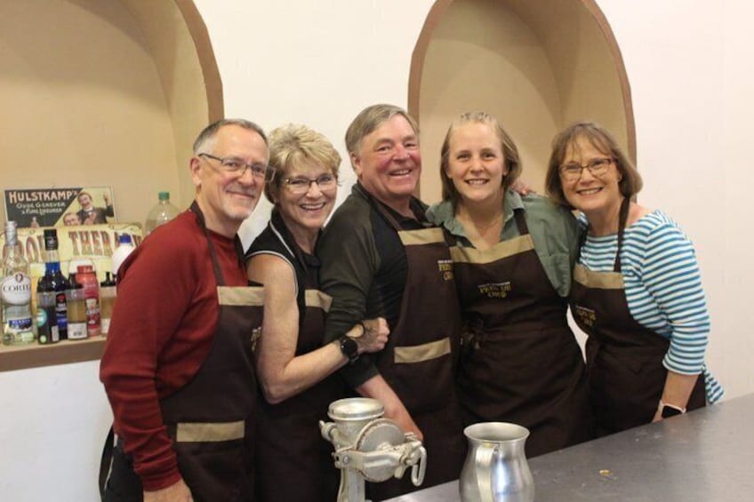 A group of people standing in a kitchen with aprons, a coffee pot, and a sign on the wall. 5