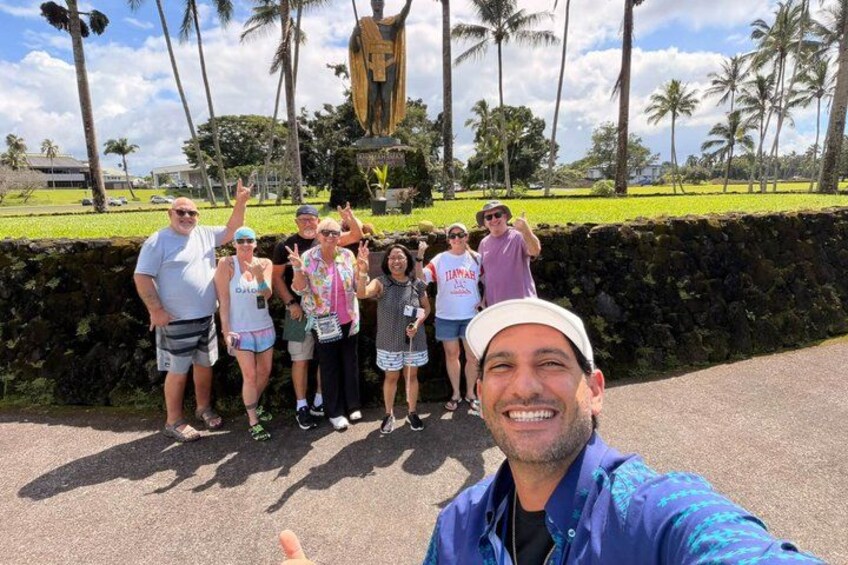 Un grupo de personas posando frente a una estatua, con un muro de piedra y palmeras al fondo. 4