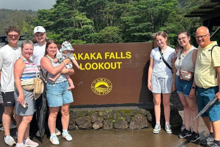 Un gruppo di persone in piedi di fronte a un cartello con la scritta 'Akaka Falls Lookout'. 2