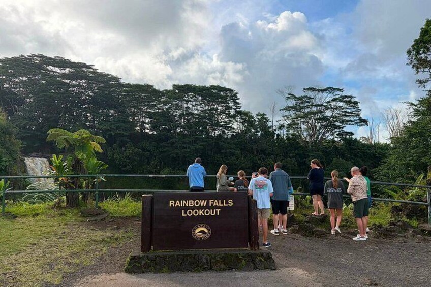 A group of people at a lookout point with a sign reading 'Rainbow Falls Lookout.' 1