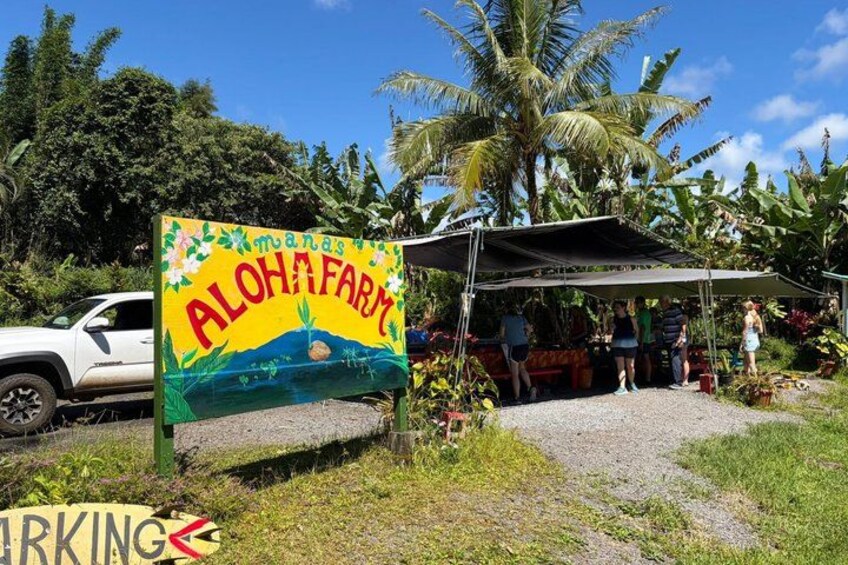 A sign for Aloha Farm, a parked white vehicle, and a covered area with people. 2