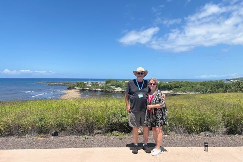 A man and a woman standing on a concrete path with a beach and ocean in the background. 1