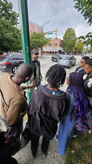 A group of people standing by a street corner, a traffic light, and parked cars. 3