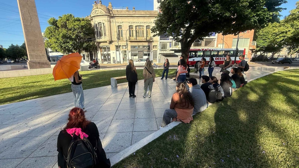 A group of people sitting on a grassy area in a public square with a historic building in the background. 5