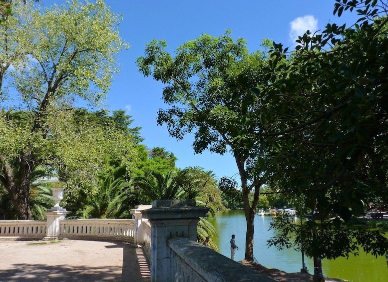 A serene park with a lake, a bridge, and a person fishing. 2