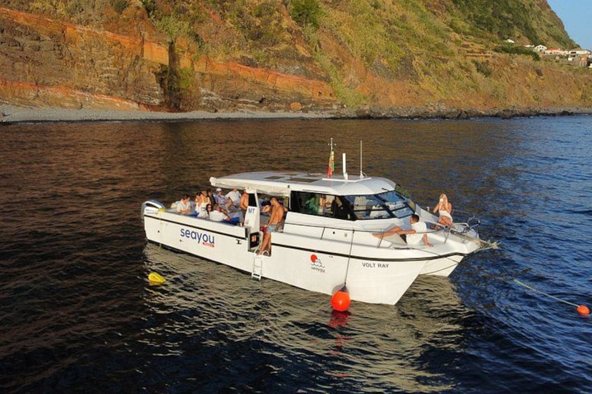 Una barca chiamata VOLT RAY con persone a bordo, che galleggia in acque calme vicino a una costa rocciosa. 4