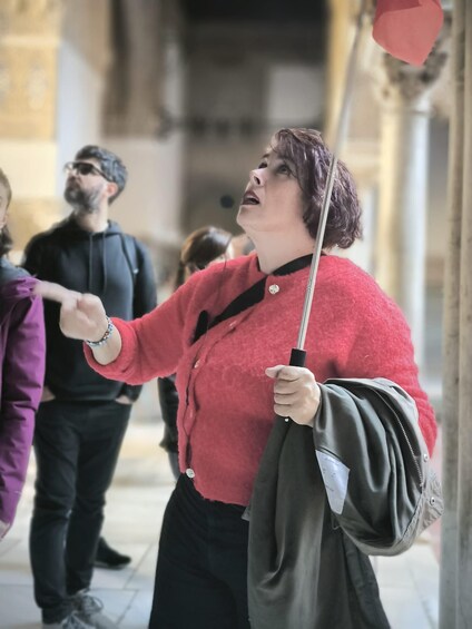 A person in a red sweater holding a wand, standing in a public space with other people around. 3