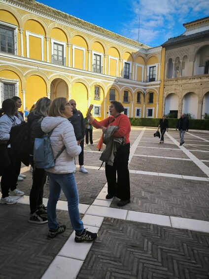 A courtyard with yellow buildings, people walking, and a woman pointing. 2