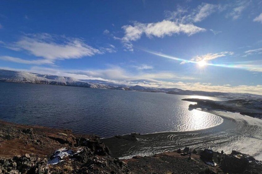 A large body of water reflecting sunlight, surrounded by rocky terrain and distant mountains. 5
