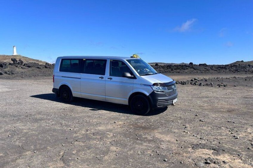 Un fourgon blanc est garé dans un paysage désolé, avec un phare en arrière-plan. 3