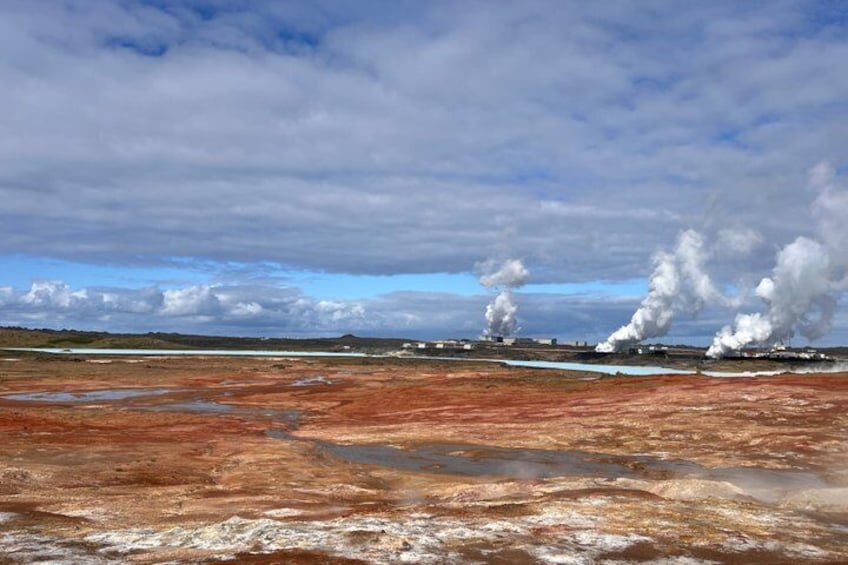 A geothermal area with steam vents, a barren landscape, and a cloudy sky. 1