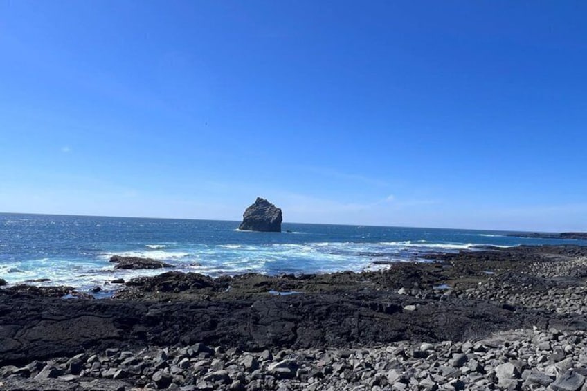 Une côte rocheuse où les vagues s’écrasent sur le rivage, et une formation rocheuse imposante qui se détache à l’horizon. 4