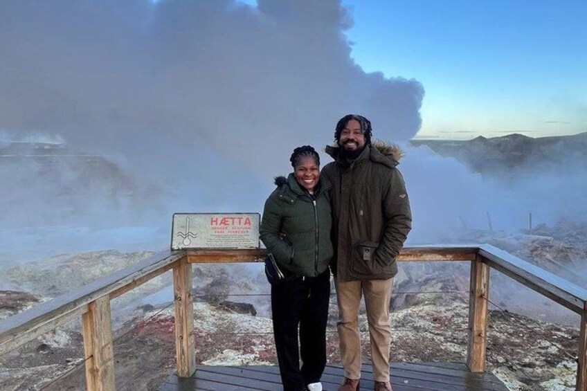 Two people standing on a wooden platform with a sign that reads 'HATTA' in the background. 3