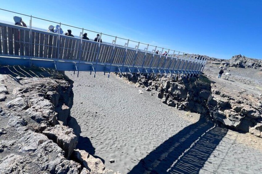 Une plage rocheuse avec une rambarde en métal, où des gens se promènent. 2