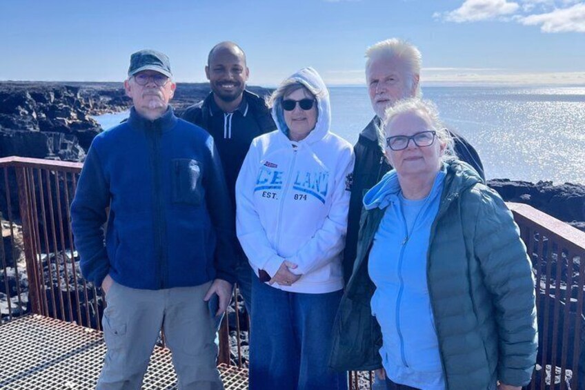 A group of people standing on a metal deck with a rocky coastline and ocean in the background. 5