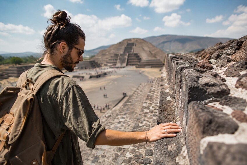 A person touching a stone wall at an ancient archaeological site with pyramids in the background. 1