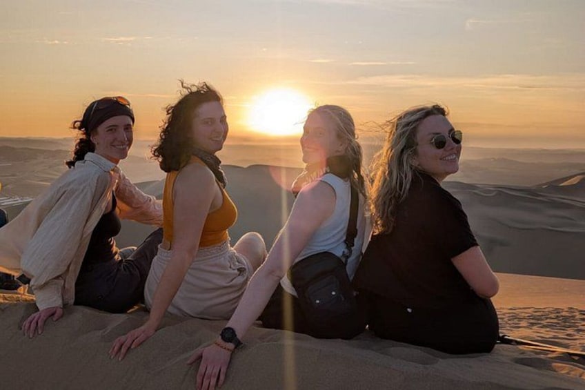 Four people sitting on sand dunes with the sun setting in the background. 3