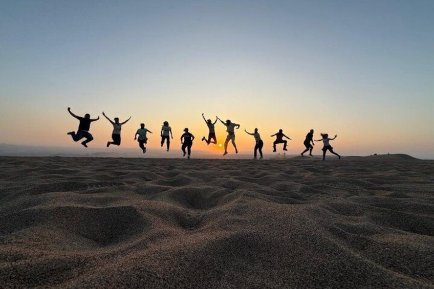 Eine Gruppe von Menschen springt bei Sonnenuntergang in einer Wüste. 2