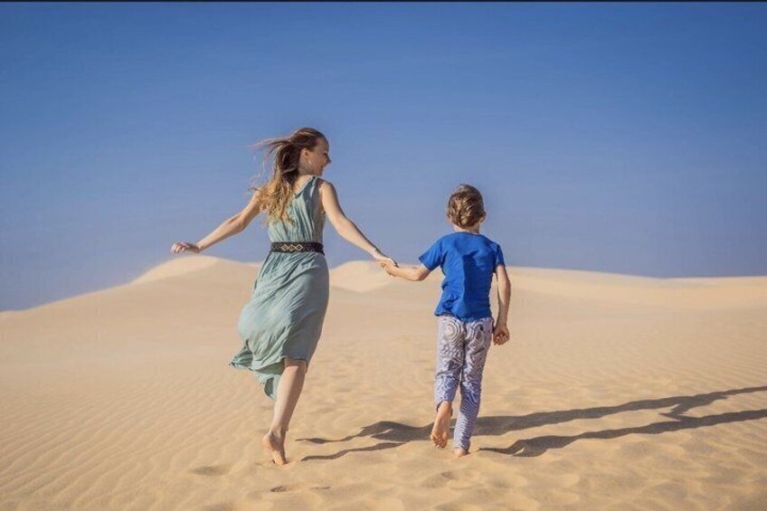 A person in a blue dress and a child in a blue shirt walking on sand dunes. 2