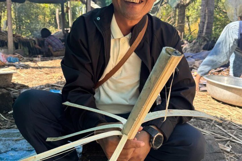 A person holding a rolled-up object, possibly a book or a scroll, sitting outdoors with a natural, wooded background. 2