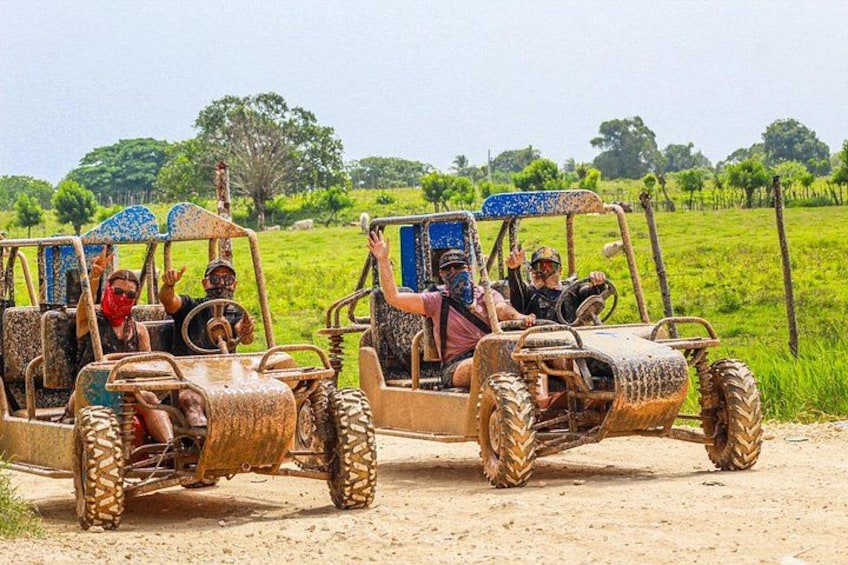 Three off-road vehicles on a dirt path with passengers, surrounded by green fields and trees. 5