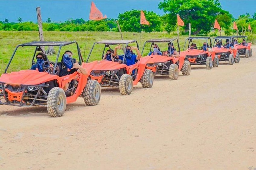 A line of orange off-road vehicles on a dirt road with flags in the background. 3