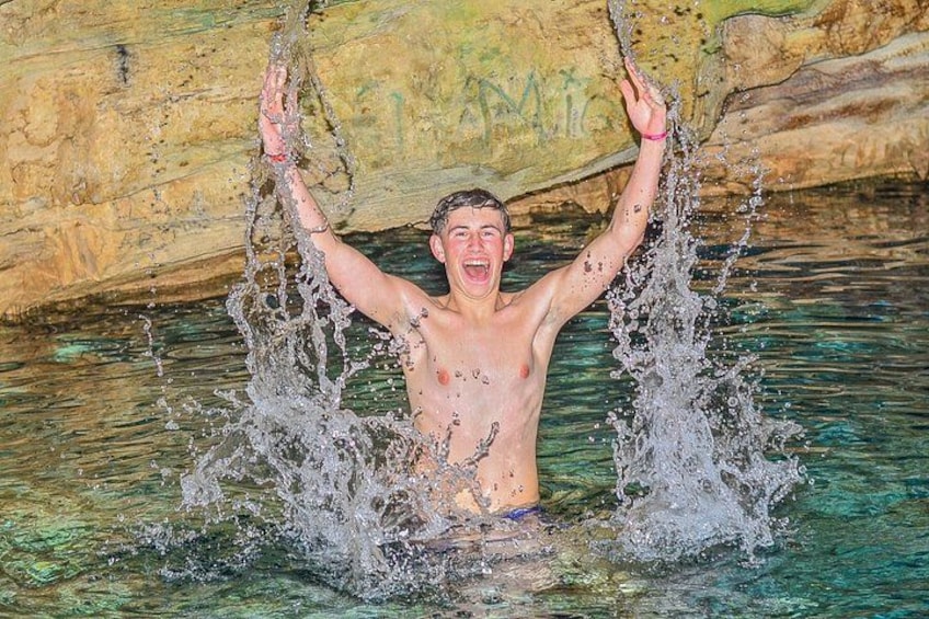 Una persona immersa nell'acqua con le braccia alzate, all'interno di una grotta rocciosa. 2