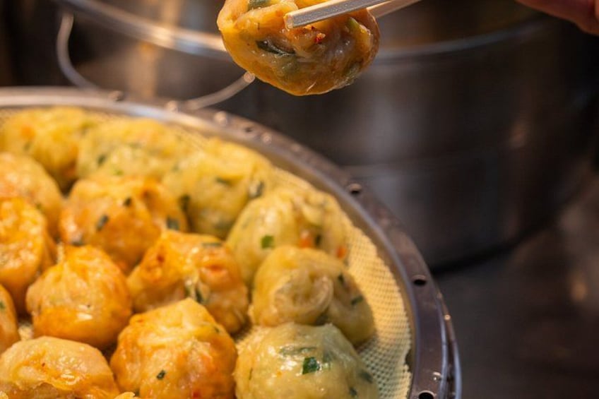 Gros plan sur des raviolis tenus avec des baguettes, avec un panier vapeur en arrière-plan. 3
