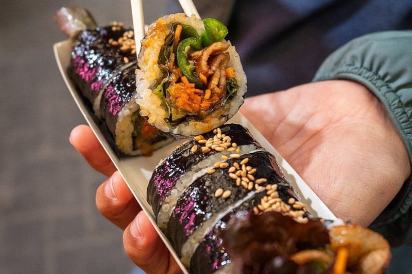 Une personne tenant une assiette de makis, dont un est en train d’être pris avec des baguettes. 5