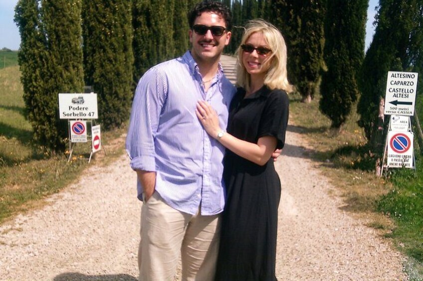 Ein Mann und eine Frau stehen auf einem Kiesweg, an dem Schilder 'Poderi Sorbello 47' und 'Alteseino Caparzo Castellet Altese' stehen. 1