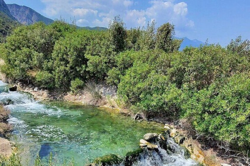 A clear river with a waterfall, surrounded by dense green vegetation and mountains in the background. 4