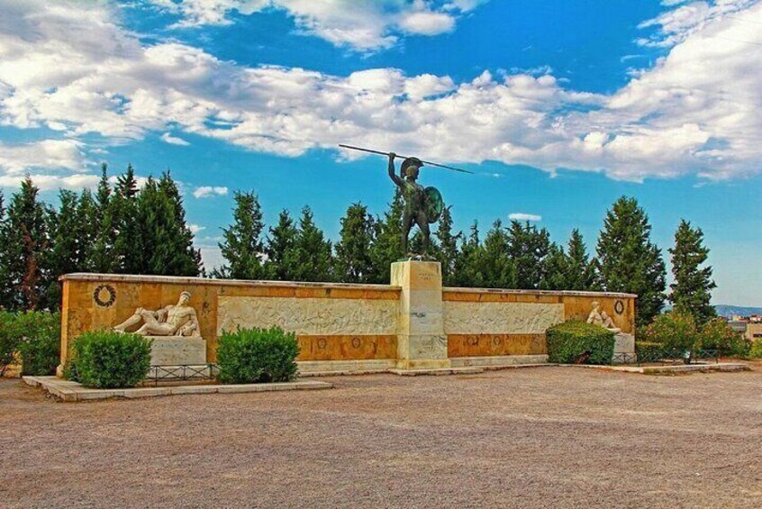 A statue of a warrior holding a spear, a relief sculpture, and a stone wall with greenery around. 5