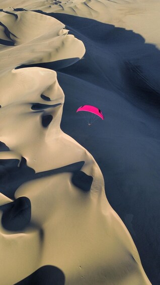 A pink parachute descending over a desert landscape with undulating sand dunes. 2